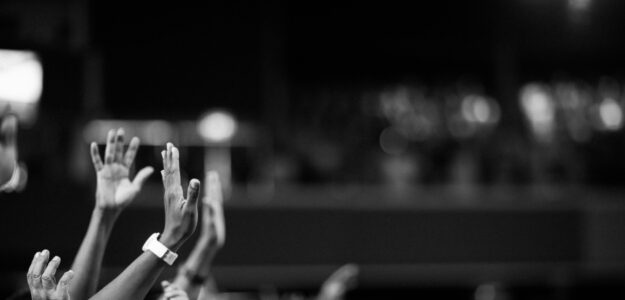 Black and white image of audience with hands raised, capturing concert energy.
